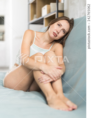 Sad adult woman sitting on sofa in living room Sad adult woman sitting on sofa in living room 142765062