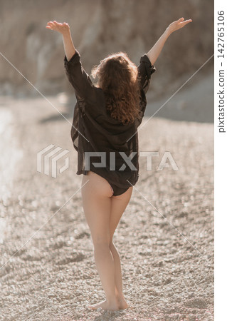 Woman beach freedom standing with arms raised on a rocky shore enjoying a sunny day of summer vacation lifestyle 142765106