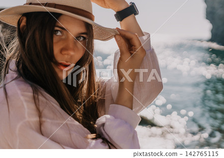 Woman ocean portrait young woman in white linen shirt adjusting her straw hat by the sea during golden hour sunset lighting Woman ocean portrait young woman in white linen shirt adjusting her straw hat by the sea during golden hour sunset lighting 142765115
