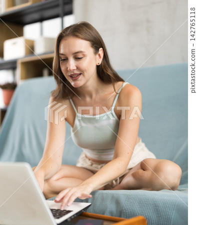 Positive adult woman working on laptop on cozy sofa Positive adult woman working on laptop on cozy sofa 142765118