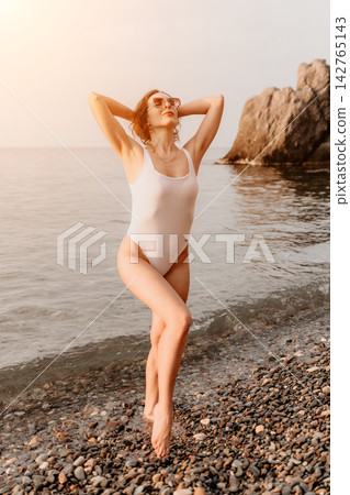 Woman Beach Swimsuit posing on a pebble shore by the ocean with scenic rocks and sunlight during a summer vacation Woman Beach Swimsuit posing on a pebble shore by the ocean with scenic rocks and sunlight during a summer vacation 142765143