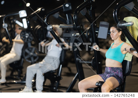 In gym, woman uses chest press machine to strengthen arm muscles In gym, woman uses chest press machine to strengthen arm muscles 142765248