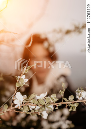 Blossom spring woman standing behind blooming tree branches in a sunny garden with soft artistic bokeh and warm light Blossom spring woman standing behind blooming tree branches in a sunny garden with soft artistic bokeh and warm light 142765309