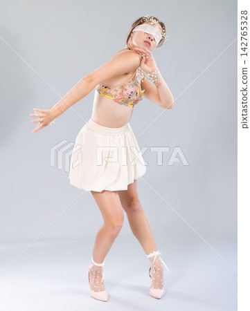 Sophisticated and elegant young woman in a chic beige dress with matching bra posing gracefully against a soft blue studio backdrop 142765328