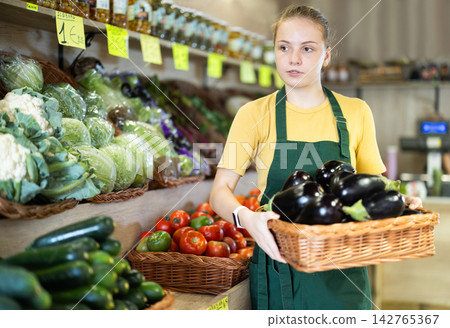 Young woman putting a basket of eggplants on display Young woman putting a basket of eggplants on display 142765367