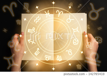 Exploration of zodiac signs with hands holding a book and symbols surrounding it Exploration of zodiac signs with hands holding a book and symbols surrounding it 142765410