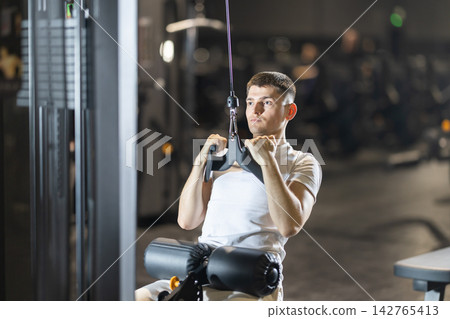 During training session in mini group of athletes, man exercises on cable crossover machine During training session in mini group of athletes, man exercises on cable crossover machine 142765413