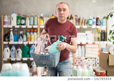 Middle-aged man placing cleaning spray into shopping basket in store Middle-aged man placing cleaning spray into shopping basket in store 142765454