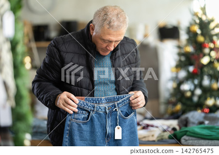 Attentive mature man choosing jeans pantaloons in clothing store 142765475