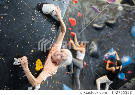 Joyful concentrated senior woman busy with her hobby bouldering, climbing on artificial wall in gym, extreme sport, rock-climbing concept Joyful concentrated senior woman busy with her hobby bouldering, climbing on artificial wall in gym, extreme sport, rock-climbing concept 142765538
