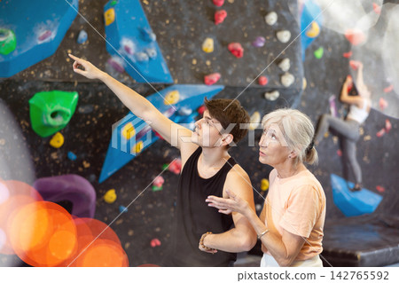 Young confident climbing instructor explaining wall climbing to mature woman Young confident climbing instructor explaining wall climbing to mature woman 142765592