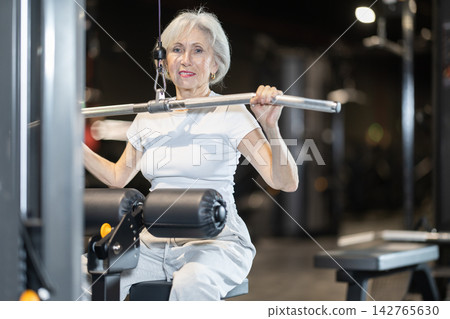 Senior woman doing wide grip lat pulldown on cable machine at gym Senior woman doing wide grip lat pulldown on cable machine at gym 142765630