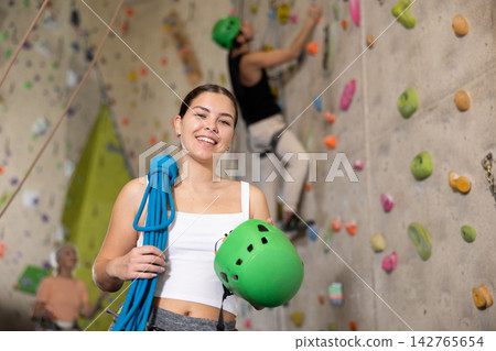 Young confident female climber with her equipment getting ready for training Young confident female climber with her equipment getting ready for training 142765654