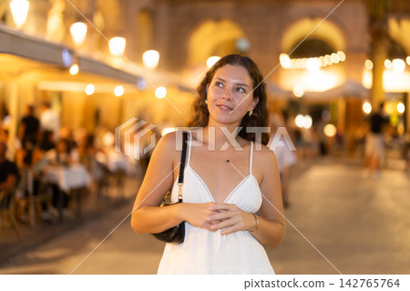 In evening, young smiling girl walks along city street Placa Real In evening, young smiling girl walks along city street Placa Real 142765764