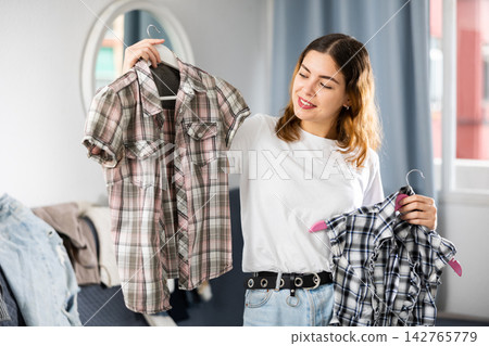 Young woman choosing right shirt to wear Young woman choosing right shirt to wear 142765779