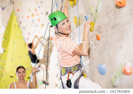 positive muscular retired woman in gym climbing up artificial rock climbing wall positive muscular retired woman in gym climbing up artificial rock climbing wall 142765869
