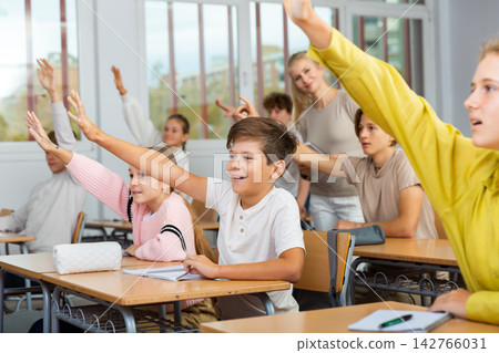 Friendly schoolchildren raise their hand to answer during lesson Friendly schoolchildren raise their hand to answer during lesson 142766031