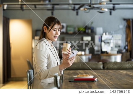 A young woman looking at her smartphone while eating breakfast at a cafe. A young woman looking at her smartphone while eating breakfast at a cafe. 142766148