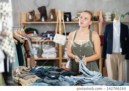 Woman standing in the store and choosing pants and shorts Woman standing in the store and choosing pants and shorts 142766260