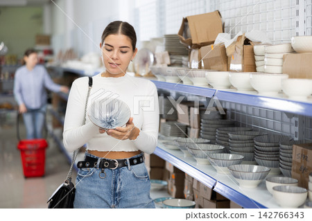 Young woman in supermarket is choosing plates with Asian pattern Young woman in supermarket is choosing plates with Asian pattern 142766343