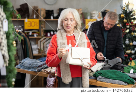 Uncertain mature woman choosing handbag in clothing store Uncertain mature woman choosing handbag in clothing store 142766382