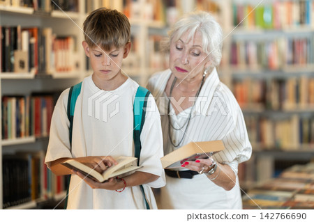 Grandmother with grandson choosing books near high shelves in bookstore Grandmother with grandson choosing books near high shelves in bookstore 142766690