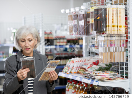 Mature woman customer chooses Chinese chopsticks in oriental goods department. Mature woman customer chooses Chinese chopsticks in oriental goods department. 142766739