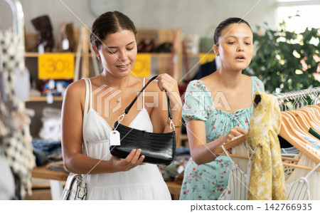 Happy young woman choosing handbag in clothing store Happy young woman choosing handbag in clothing store 142766935
