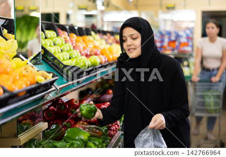 Asian woman in dark blue hijab in greengrocer s shop,picking bell pepper in small package Asian woman in dark blue hijab in greengrocer s shop,picking bell pepper in small package 142766964