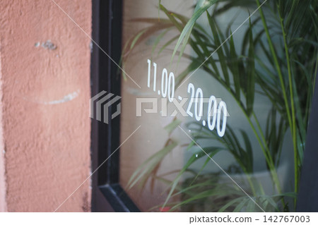 Business hours displayed on window with plants in background Business hours displayed on window with plants in background 142767003