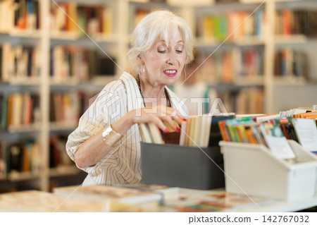 Happy senior woman choosing books from display case in bookstore Happy senior woman choosing books from display case in bookstore 142767032
