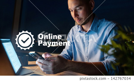 Man makes online payment at night while sitting at a table with a laptop and a plant Man makes online payment at night while sitting at a table with a laptop and a plant 142767034