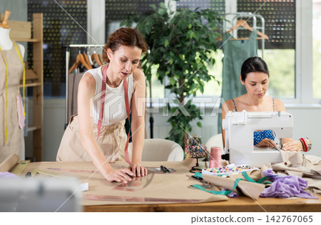 Woman tailor draw dress pattern with curve ruler on paper, female master seamstress sewing Woman tailor draw dress pattern with curve ruler on paper, female master seamstress sewing 142767065