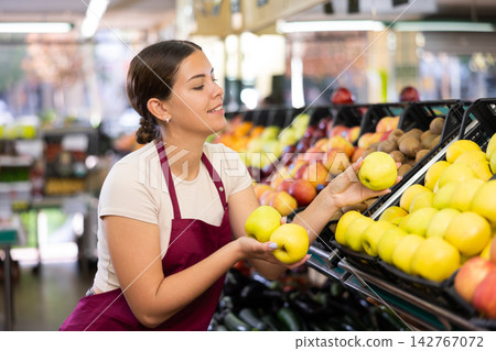 Female supermarket salesperson setting out apples on shelves Female supermarket salesperson setting out apples on shelves 142767072