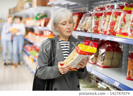 Senior woman in supermarket buys daily groceries, pasta Chinese noodles Senior woman in supermarket buys daily groceries, pasta Chinese noodles 142767074