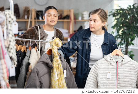 Two focused female clients carefully looking something for autumn-winter season in clothing mall Two focused female clients carefully looking something for autumn-winter season in clothing mall 142767238