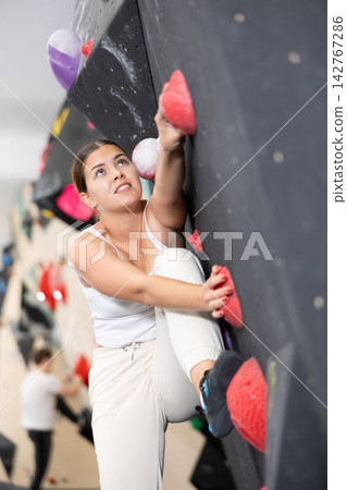 Europian girl focused on climbing to top of artificial bouldering wall along complicated route track 142767286