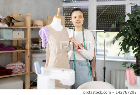 Young female dressmaker working with mannequin in sewing workshop Young female dressmaker working with mannequin in sewing workshop 142767292