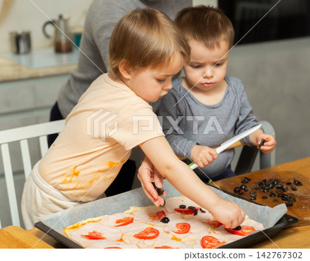 Mother and two young boys making pizza together in home kitchen Mother and two young boys making pizza together in home kitchen 142767302