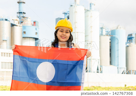 Happy young woman in helmet holding flag of Laos against background of factory Happy young woman in helmet holding flag of Laos against background of factory 142767308