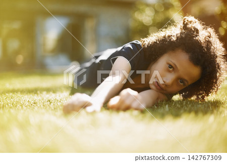 Portrait, sunshine and boy on grass, play and nature with fun, weekend break and relaxing. Face, outdoor and kid in garden, child and summer with boredom, casual and cute with youth and chilling 142767309