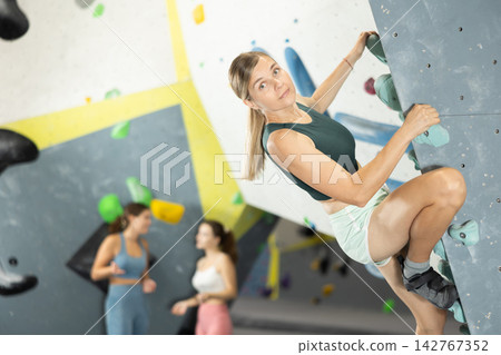 Woman climbs artificial wall bouldering, working out in gym Woman climbs artificial wall bouldering, working out in gym 142767352