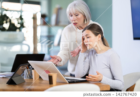 Female mature boss yells at woman employee, staff work at computer Female mature boss yells at woman employee, staff work at computer 142767420