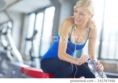 Fitness, music and water to relax with woman in gym, thinking about health, wellness or workout. Break, exercise and hydration with happy young person at training center for physical improvement Fitness, music and water to relax with woman in gym, thinking about health, wellness or workout. Break, exercise and hydration with happy young person at training center for physical improvement 142767486