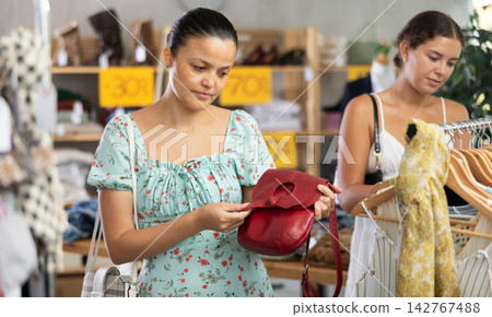 Near rack, Asian woman buys lady handbag, female client in background 142767488