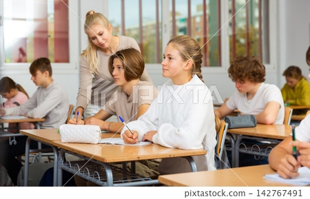 Boys and girls sitting at desk in classroom full of pupils during lesson 142767491