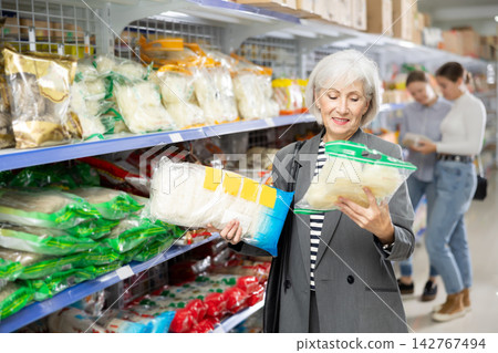 Senior woman in supermarket buys daily groceries, pasta Chinese noodles Senior woman in supermarket buys daily groceries, pasta Chinese noodles 142767494