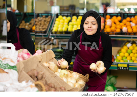 Young woman in hijab selling onions in grocery store Young woman in hijab selling onions in grocery store 142767507