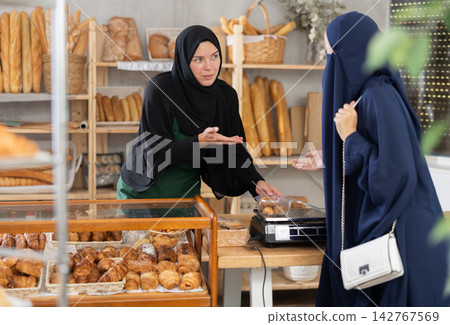 Muslim bakery worker serving female customer freshly baked pastries Muslim bakery worker serving female customer freshly baked pastries 142767569