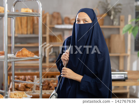 Middle-aged Muslim woman chooses some pastry in bakery Middle-aged Muslim woman chooses some pastry in bakery 142767636